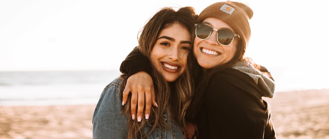 two-female-friends-hugging-smiling-at-beach