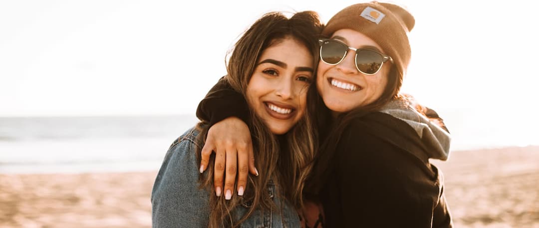 two-female-friends-hugging-smiling-at-beach