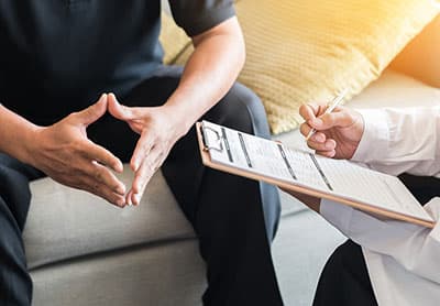 Doctor consulting male patient, working on diagnostic examination on men's health disease or mental illness, and writing on prescription record information document in clinic or hospital office