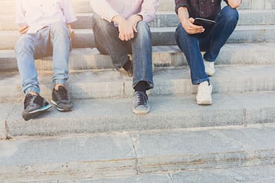 Company of three unrecognizable guys have rest on stairs in street.