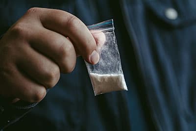 Mans hand holds plastic packet with drug powder.